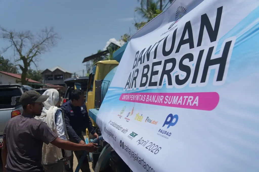 Banner on a truck promoting flood relief in Sumatra, with people standing nearby and blue sky in the background (text includes 'BANJIR' and 'UNTUK PENYINTAS BANJIR SUMATERA').